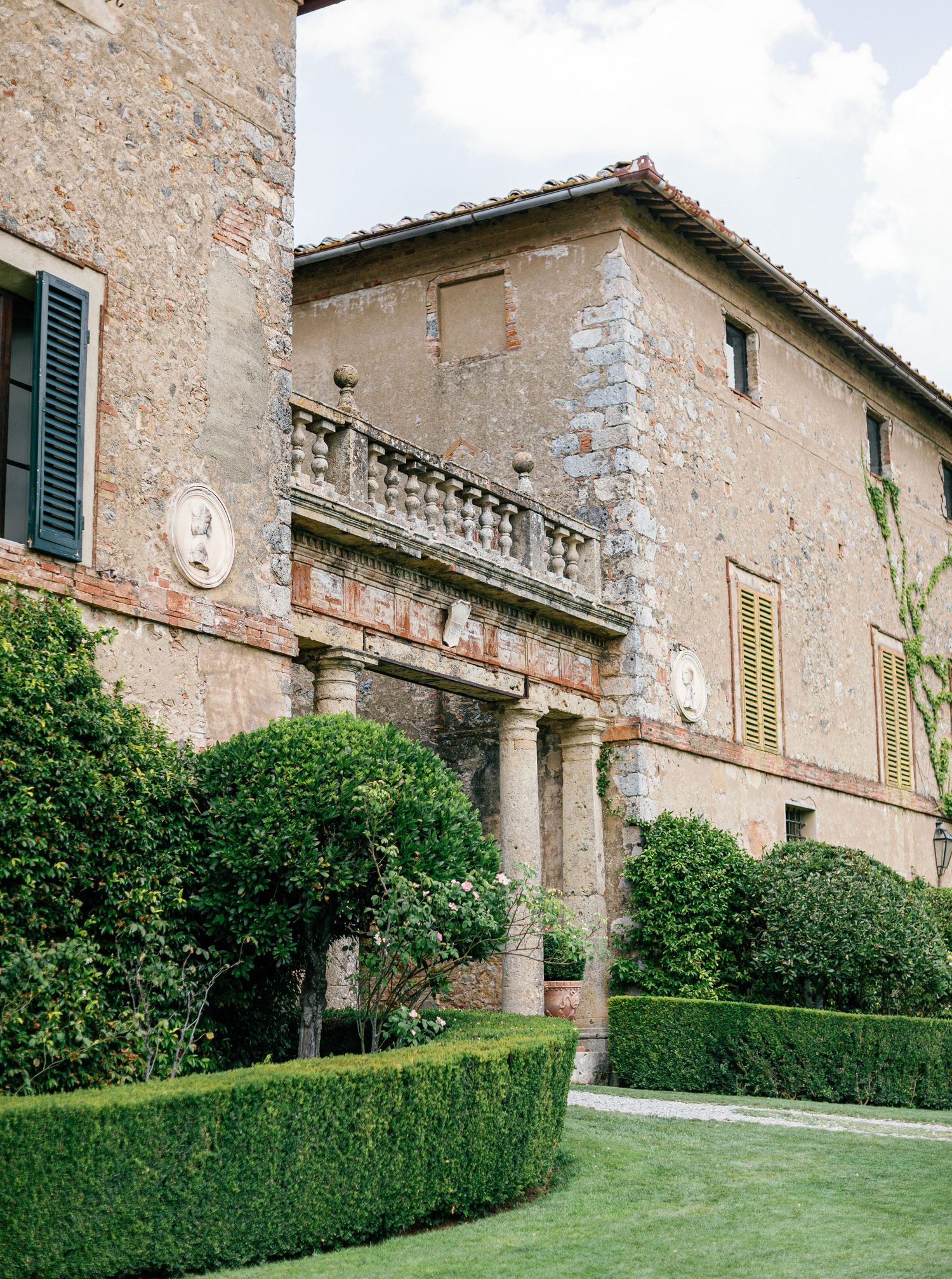 Italian villa Borgo Stomennano enexterior with stone walls, ornate balcony, green hedges  in soft afternoon light.