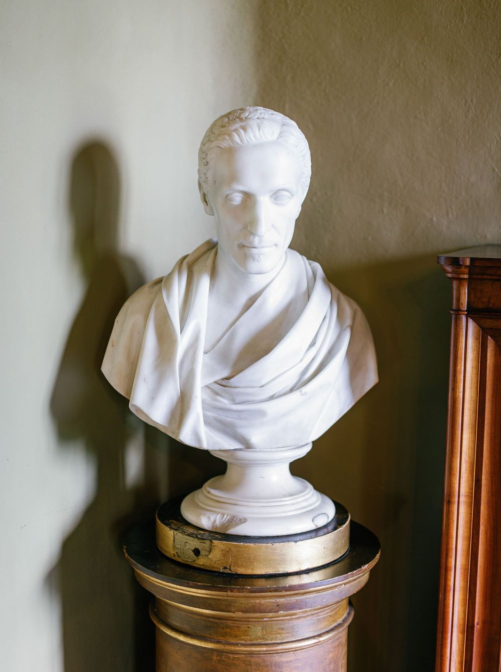 A sequence of classical white marble busts displayed on wooden pedestals shows a striking progression against a plain wall.