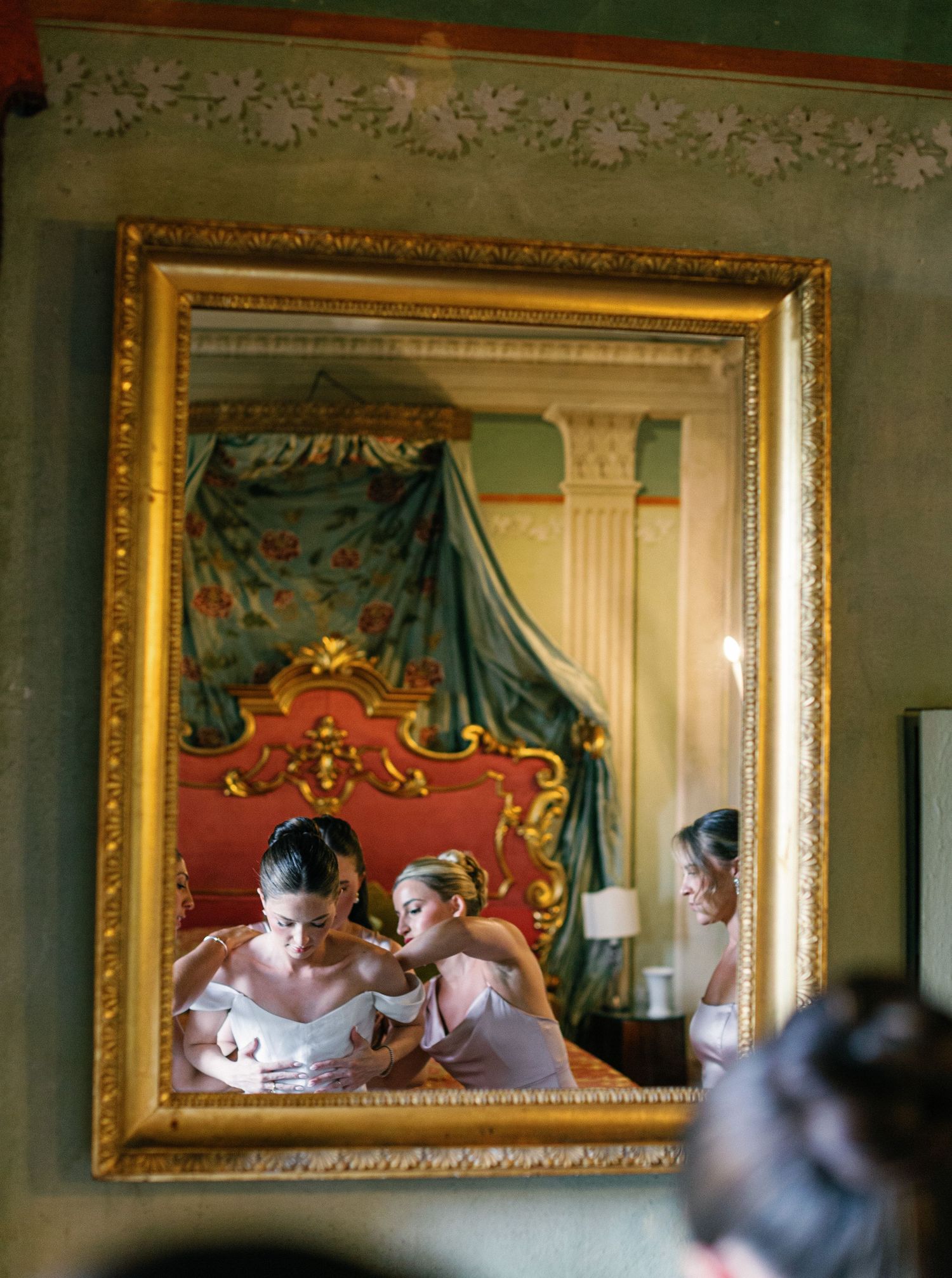 A series of ornate gilded mirrors hang on a mint green wall in a luxurious historic interior setting.