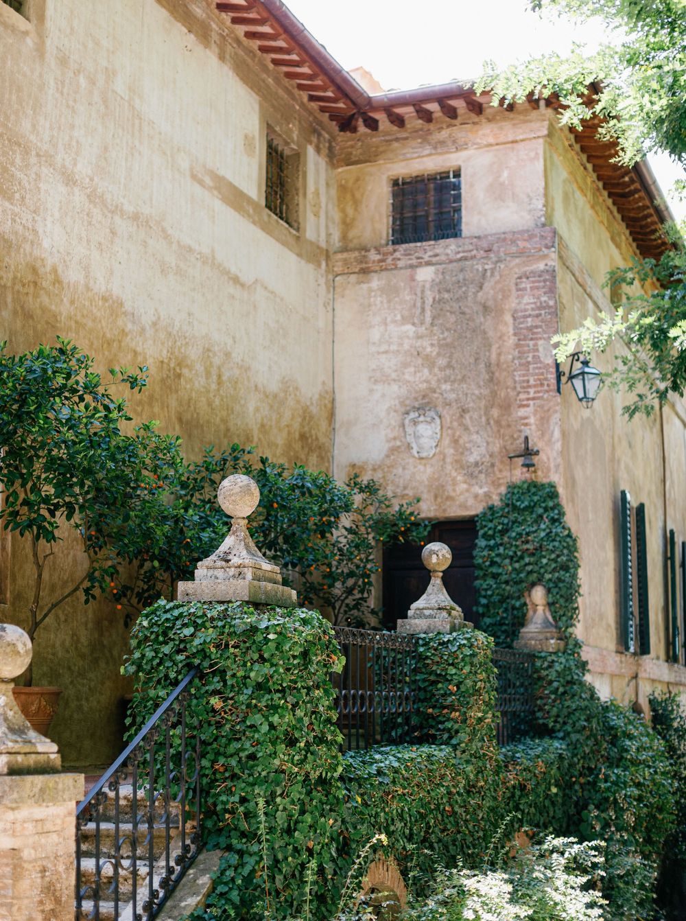 Tuscan-style villa exterior with cream stucco walls and decorative wrought iron gates surrounded by lush green landscaping.