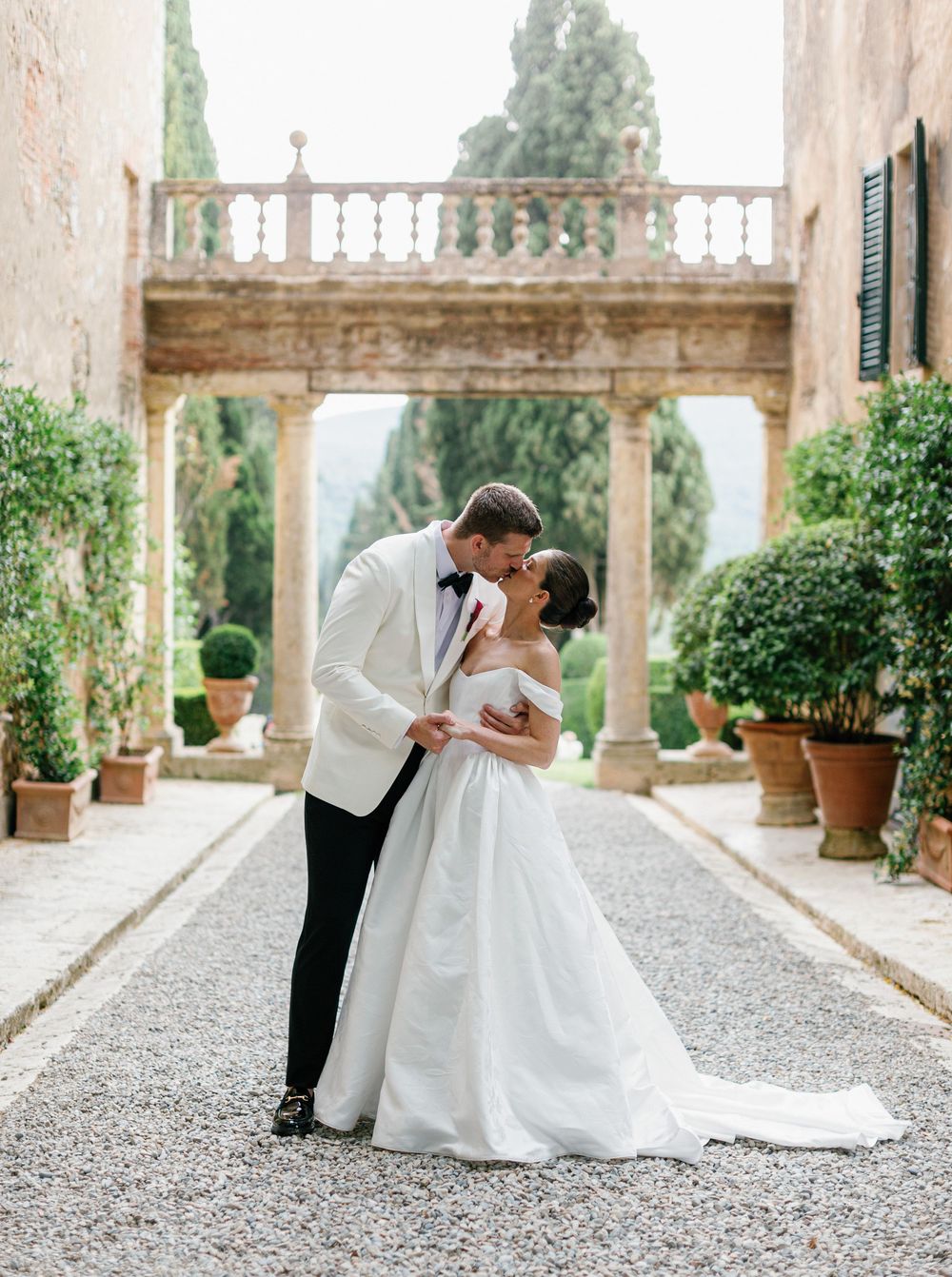 A romantic wedding couple shares intimate dips and kisses along a beautiful stone terrace with garden views and columns at Borgo Stomennano.