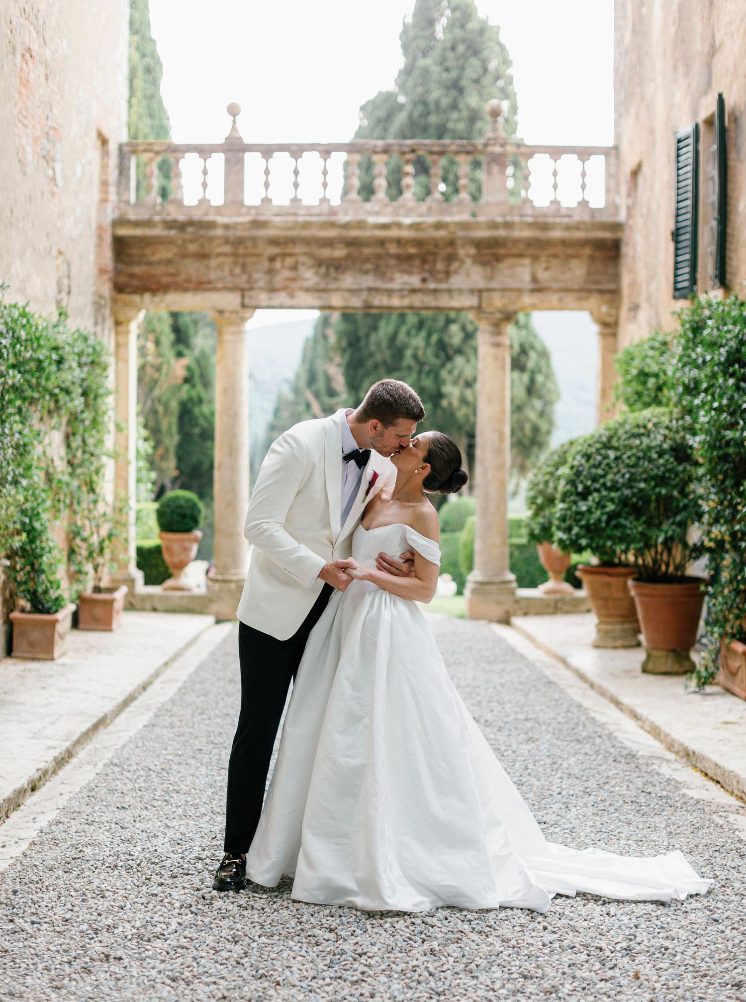 A romantic wedding couple shares intimate dips and kisses along a beautiful stone terrace with garden views and columns at Borgo Stomennano.