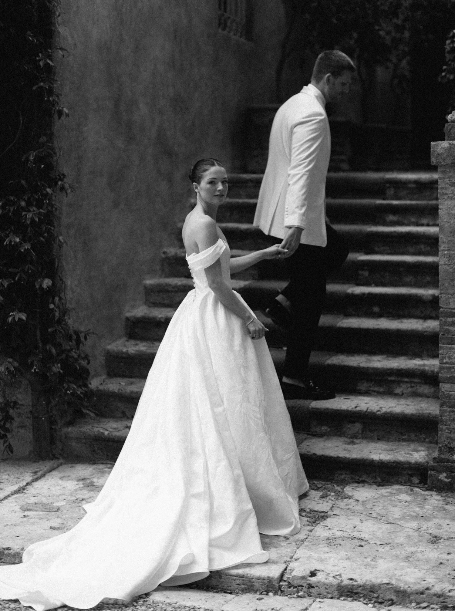 A series of black and white photos showing an elegant white wedding dress flowing down stone steps.