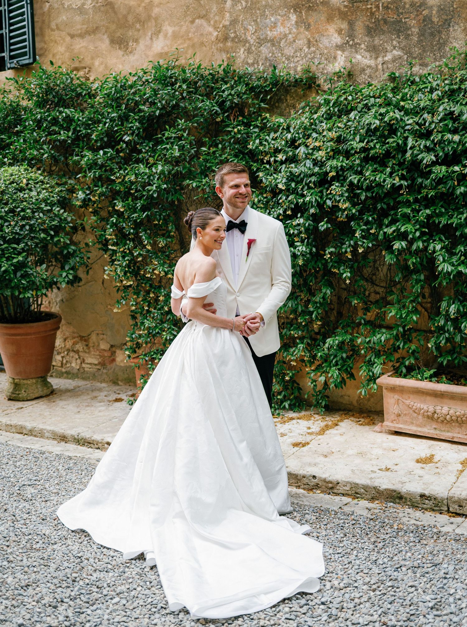 A romantic wedding couple shares an intimate moment in front of an ivy-covered stone wall during their Tuscan celebration.