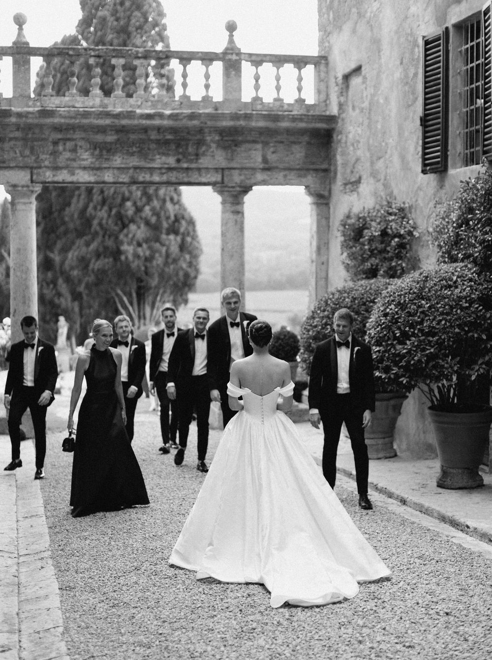 Wedding party gathered in a formal Italian courtyard at Borgo Stomennano with guests in black tuxedos and elegant white gowns.