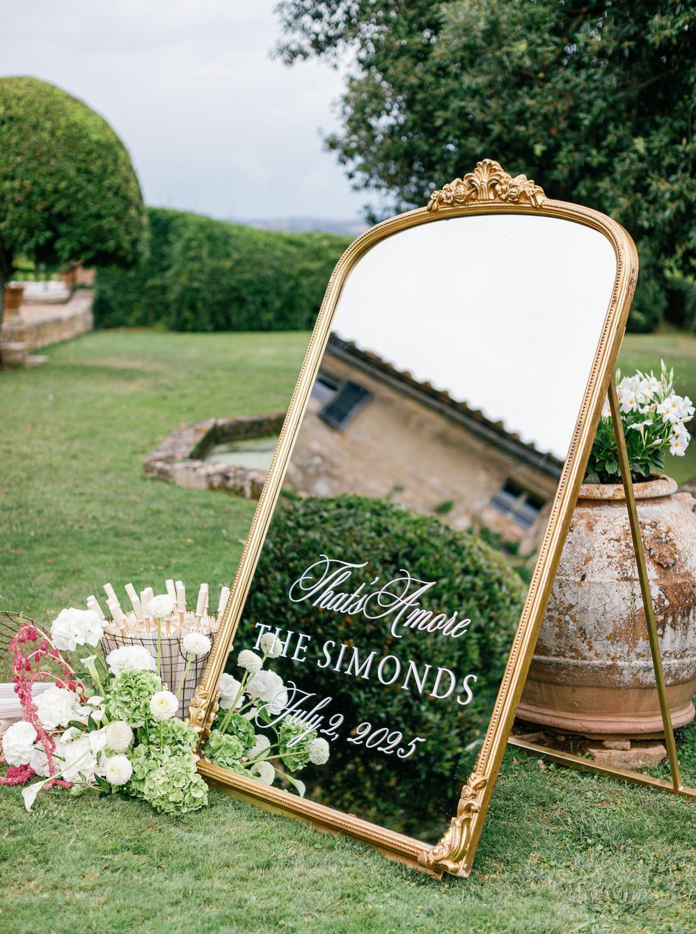 A collection of ornate gold frames displays wedding signage and decorations on grassy outdoor terrain.
