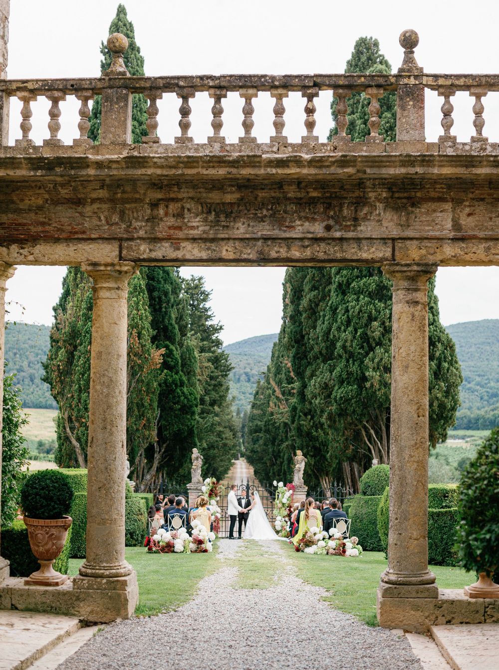 Ancient stone colonnade at a historic Italian villa Borgo Stomennano with cypress trees and scenic mountain views in the background.