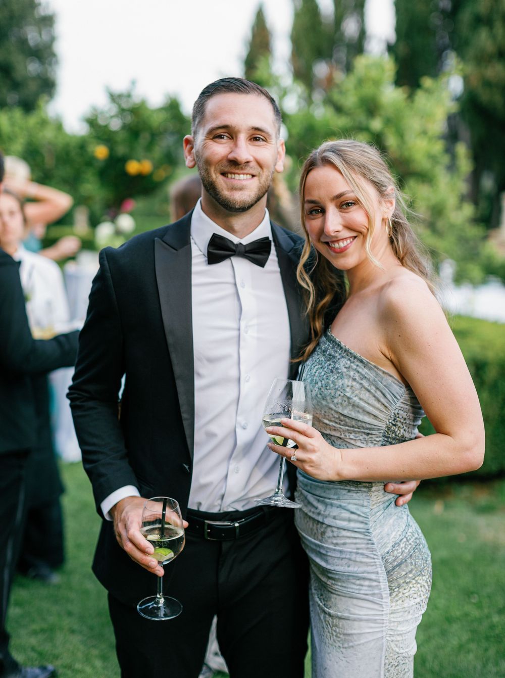 A couple in formal attire, with the woman wearing a sparkly silver gown, share intimate moments at an outdoor event.