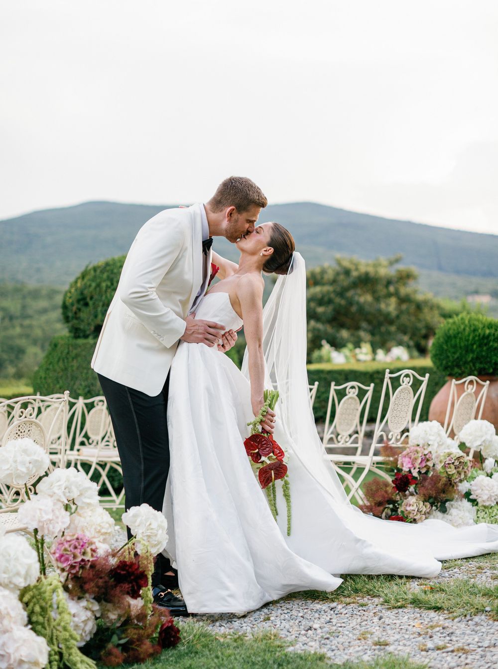Romantic outdoor Borgo Stomennano wedding ceremony setup with white chairs and floral arrangements of hydrangeas and roses.