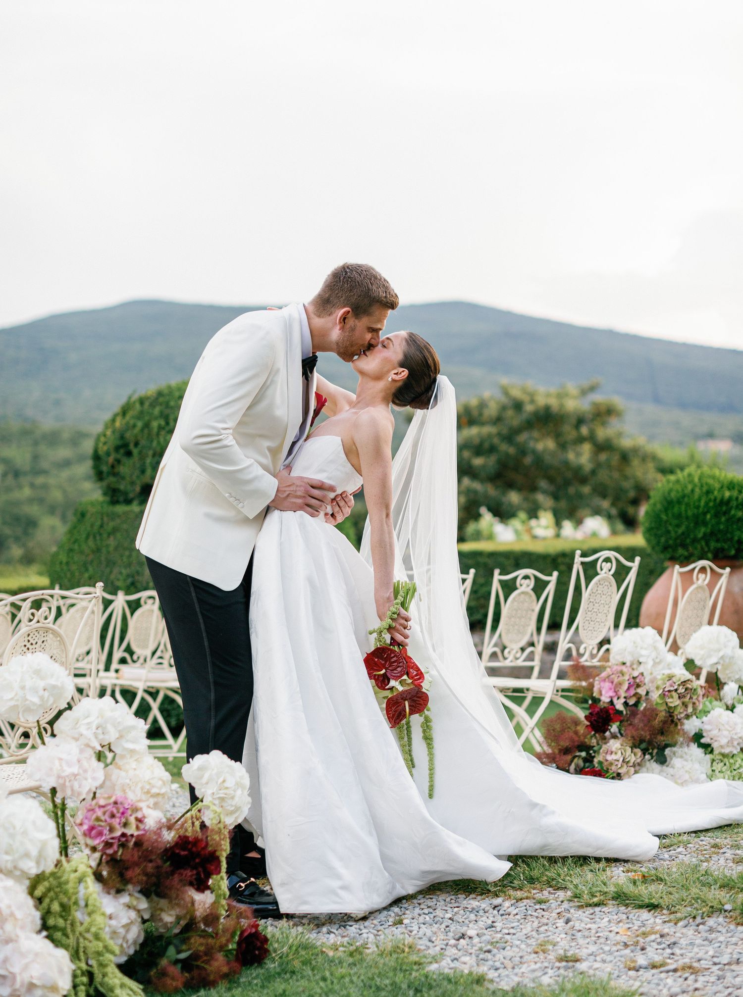 Romantic outdoor Borgo Stomennano wedding ceremony setup with white chairs and floral arrangements of hydrangeas and roses.