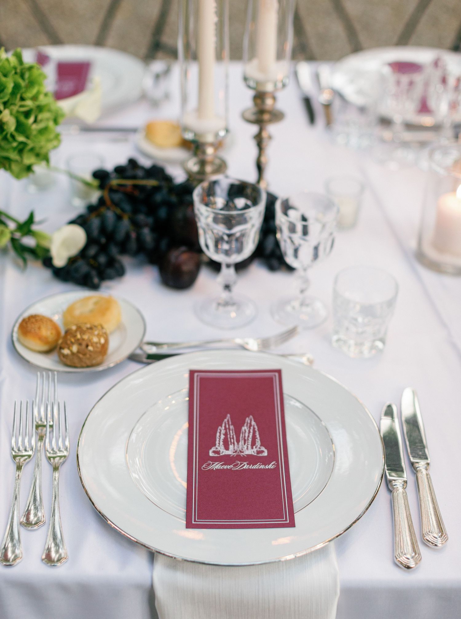 Elegant table settings with burgundy napkins and menus displayed on white plates at a formal dinner event.