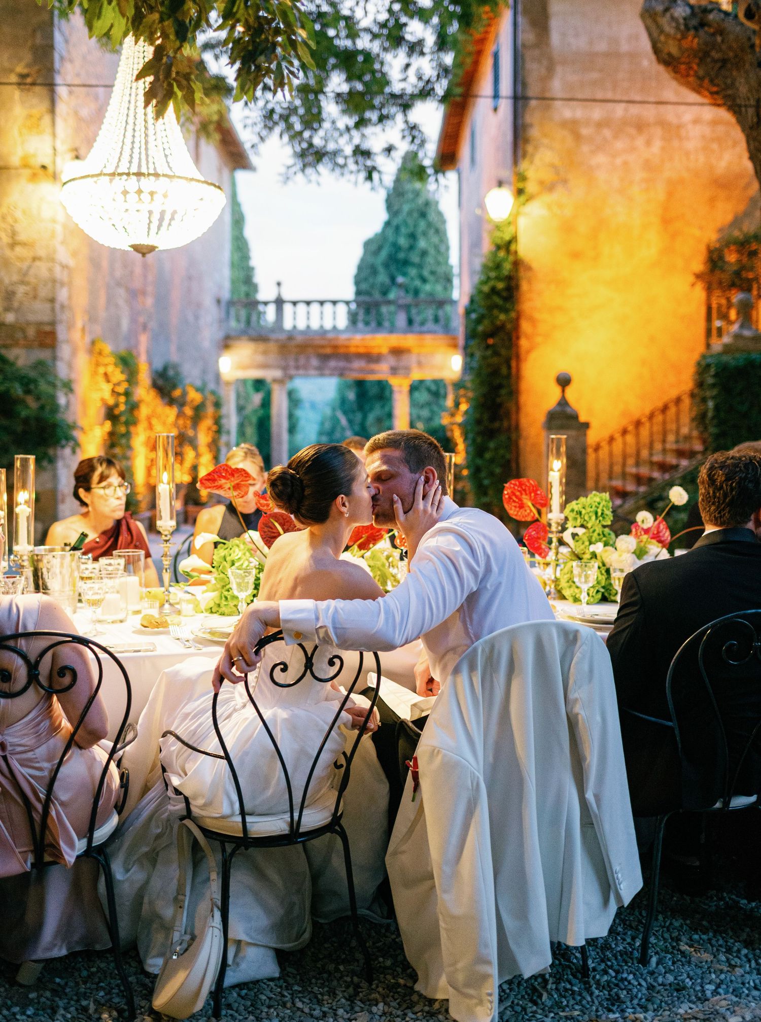 Elegant outdoor wedding reception at dusk with chandeliers and wrought iron chairs in a Borgo Stomennano villa courtyard.