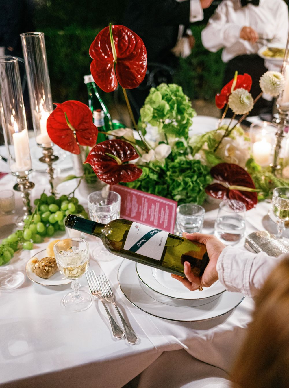 Elegant wedding table setting with crystal glassware, white linens, and red anthurium floral centerpieces.