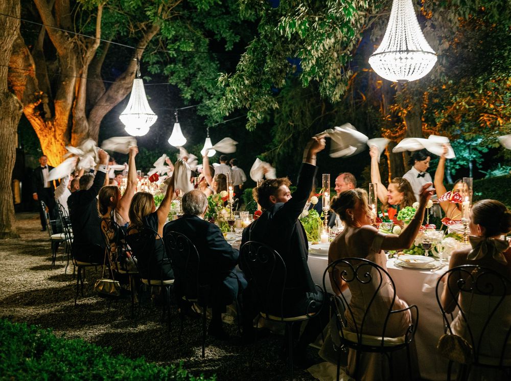 A string of elegant outdoor wedding receptions at night with chandeliers hanging from trees and guests dining al fresco at Borgo Stomennano.