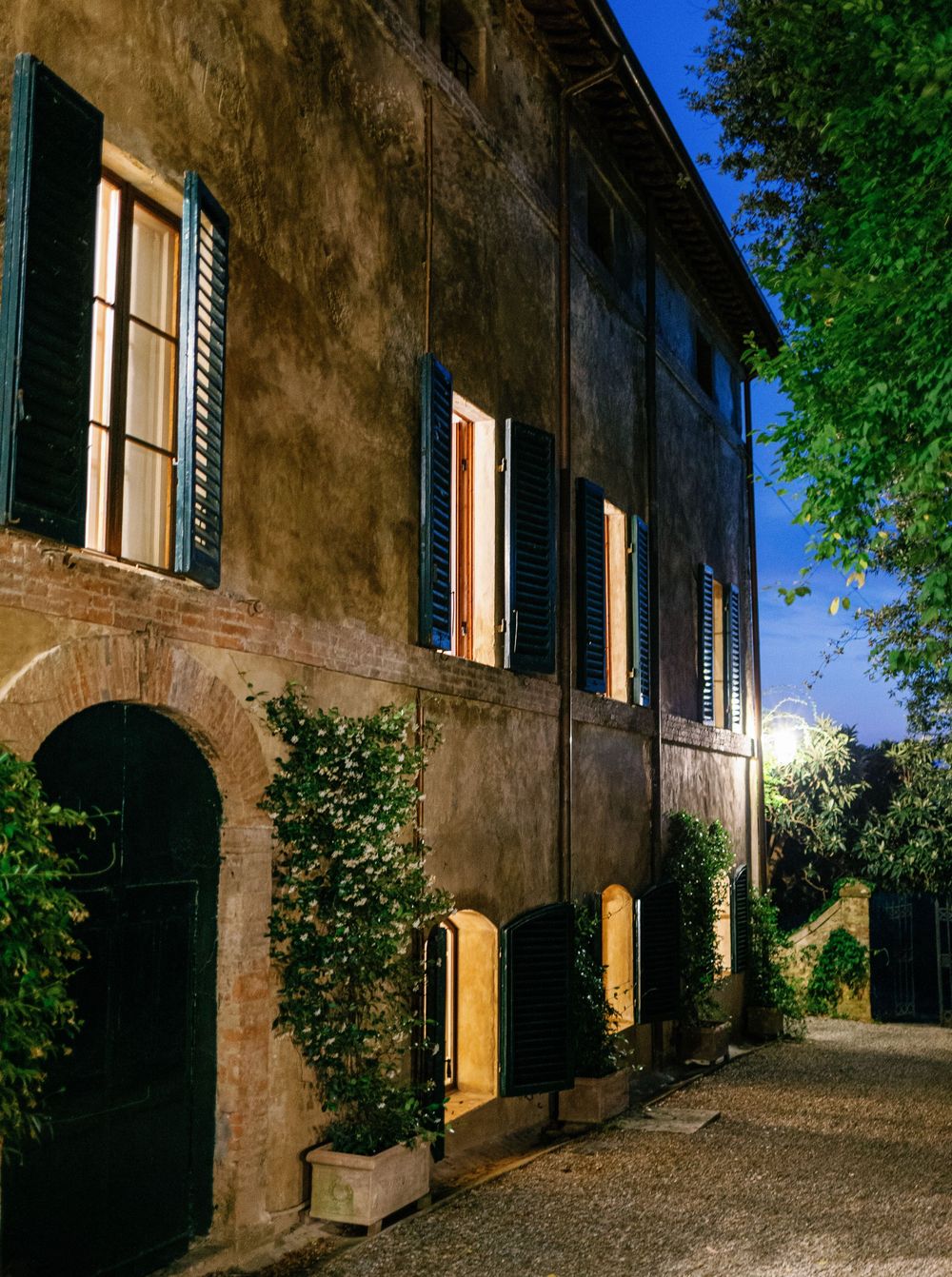 Borgo Stomennano with rustic stone walls and yellow shuttered windows along cobblestone path at dusk.