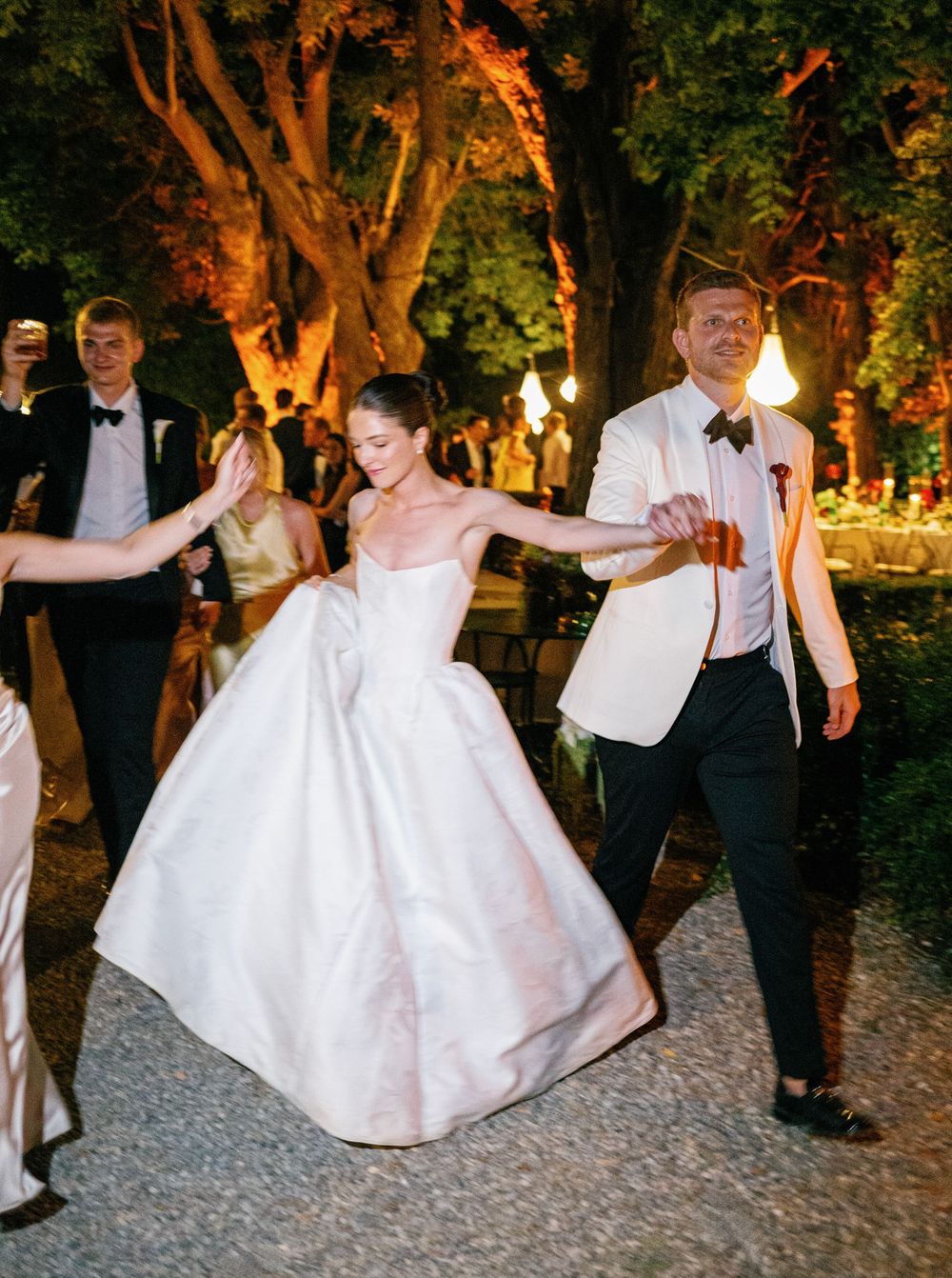 Newlyweds dancing outdoors at a wedding reception illuminated by warm evening lights in a romantic garden setting.