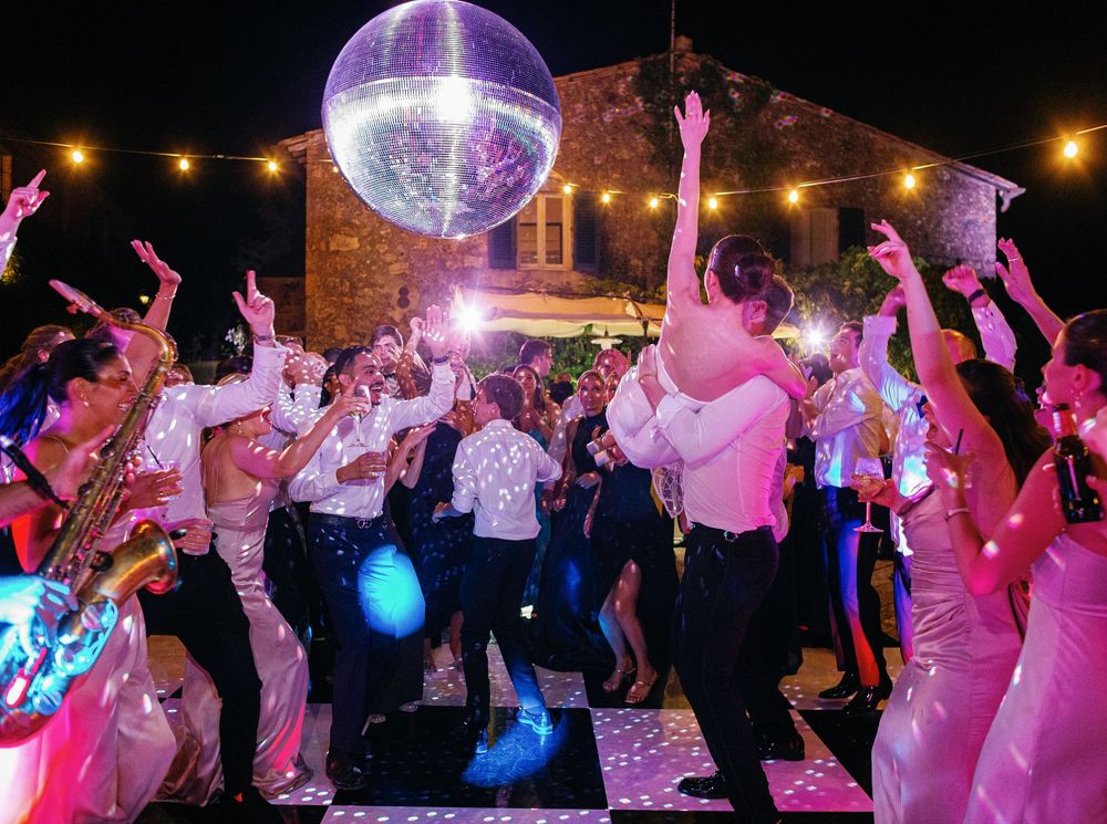People dance under a sparkling disco ball at a lively party with string lights and colorful lighting effects at Borgo Stomennano.