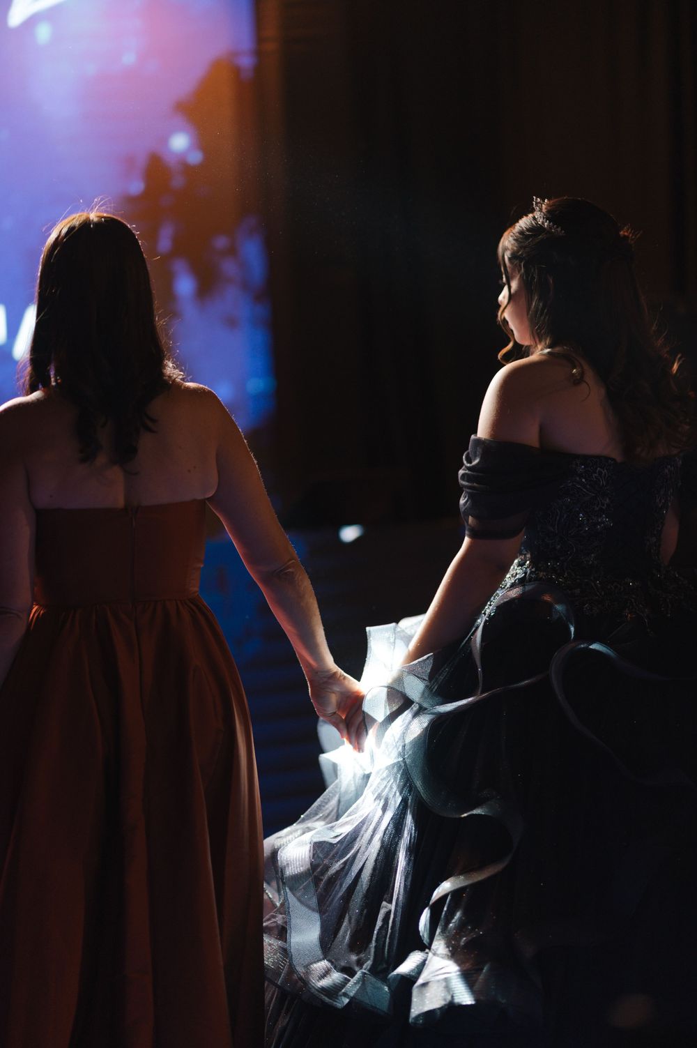 Silhouetted figures in formal attire dance together in a dimly lit ballroom with blue lighting effects in the background.