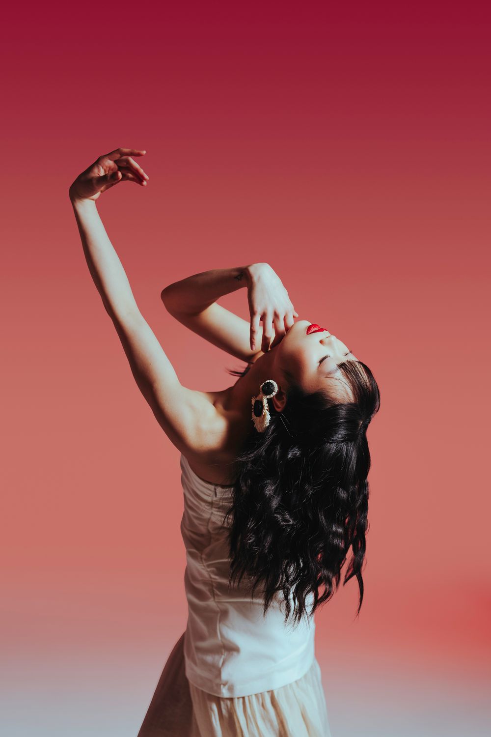 A person in a white top dances expressively against a red gradient background with cascading dark hair in motion.