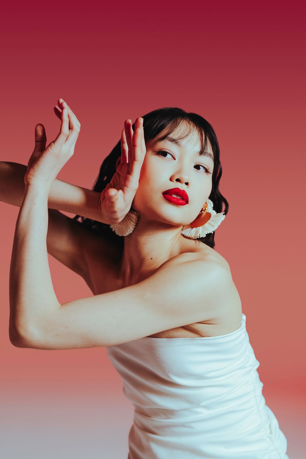 Person in a white sleeveless top poses dynamically against a red gradient background in a sequence of artistic shots.