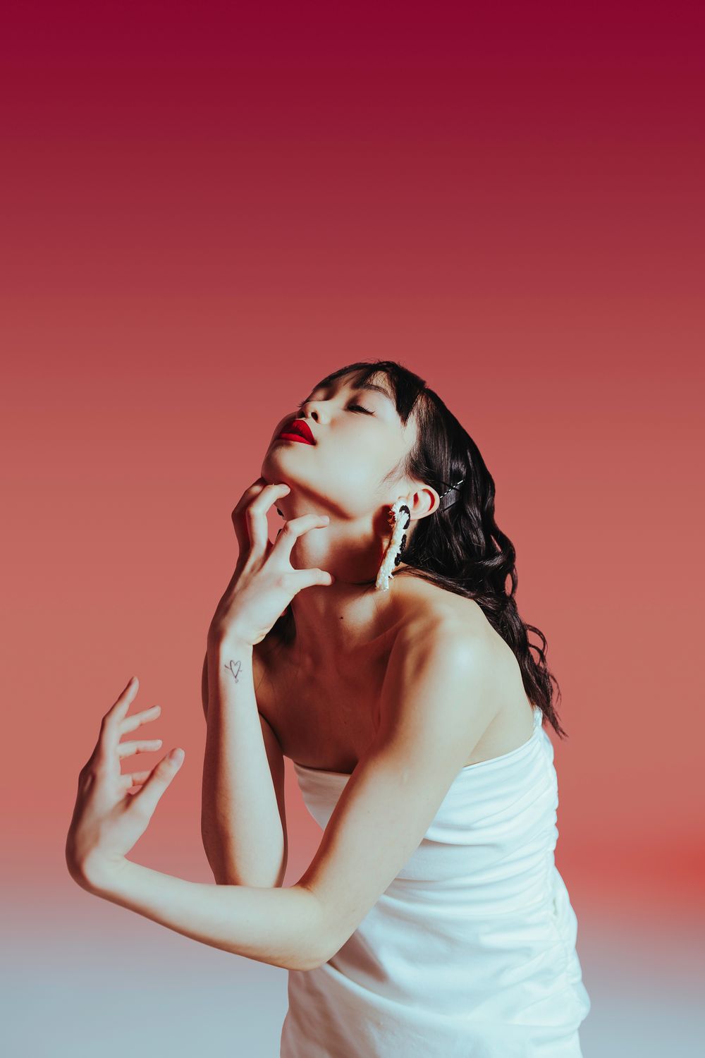 Artistic portrait series showing an individual in a white top posed against a red background with dramatic lighting effects.