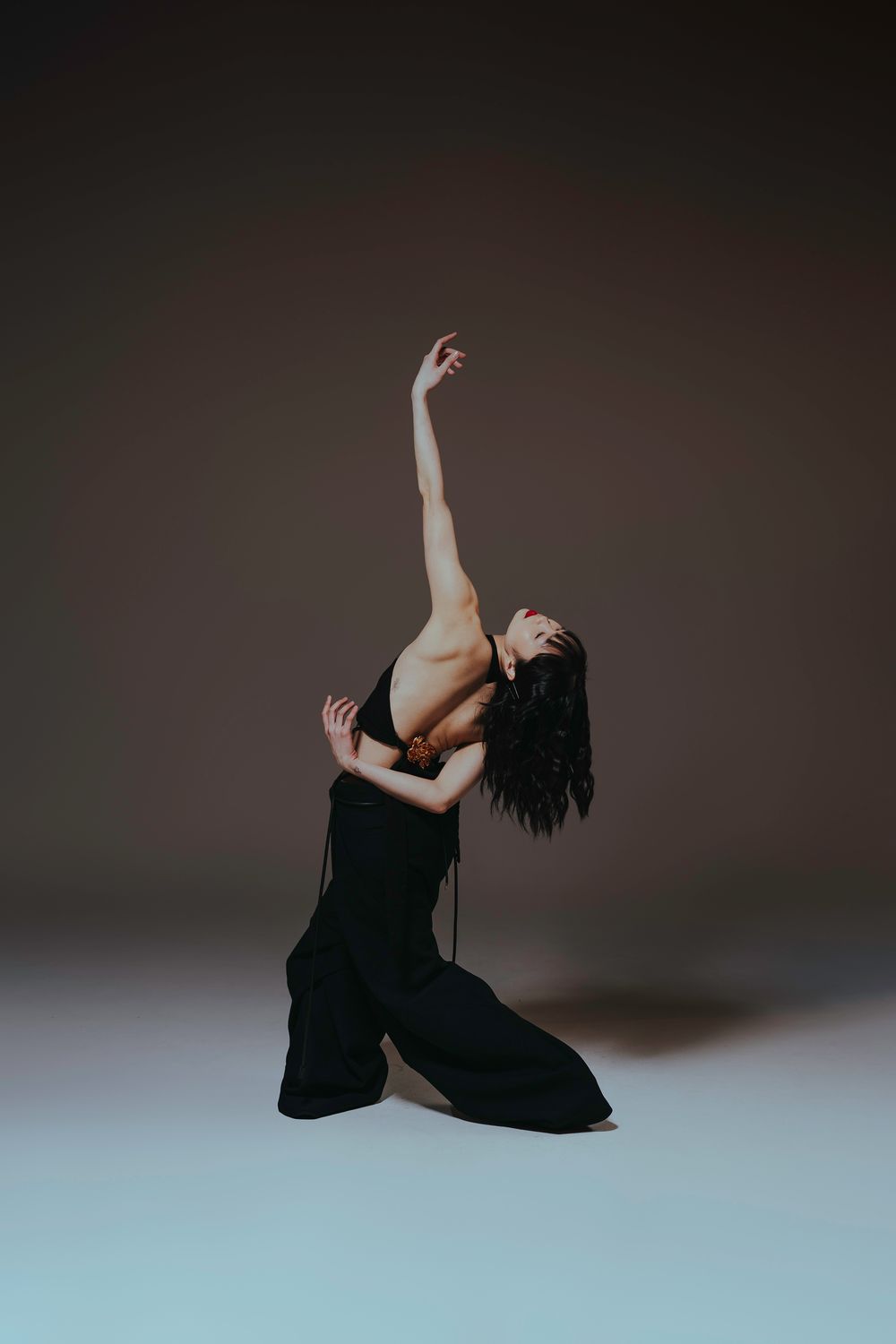 A figure in dark clothing performs an expressive contemporary dance sequence in a minimalist studio setting.