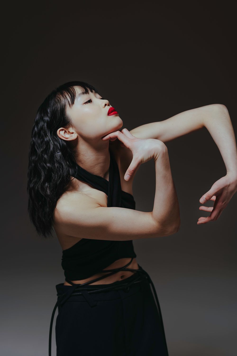 Artistic portrait series showing figure in black dress making expressive poses with hands against dark background.