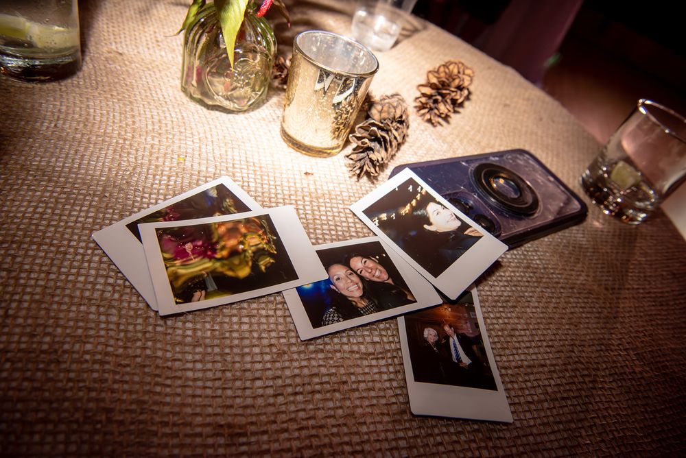 Vintage Polaroid photographs scattered on a rustic wooden table with dramatic lighting and pinecone decorations.