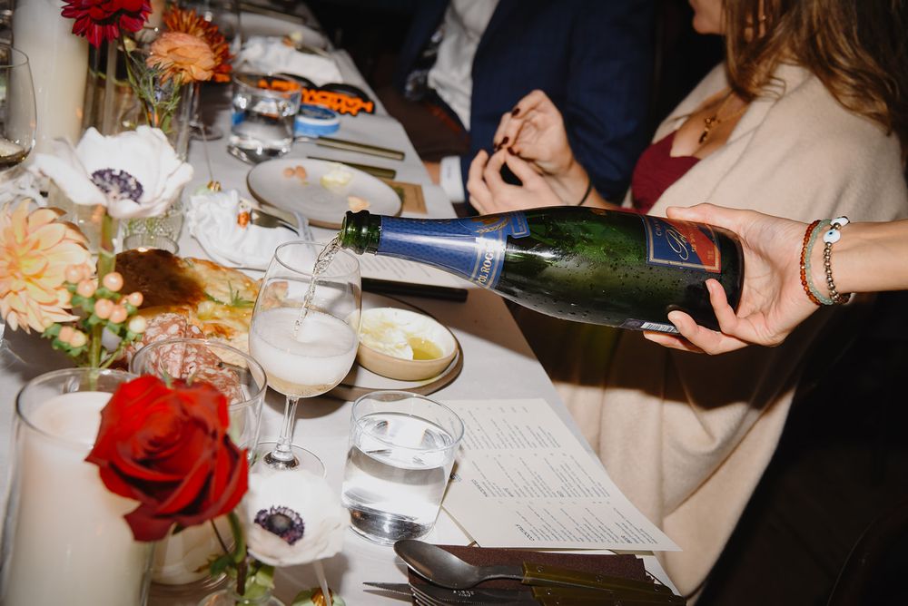 Elegant table setting at a dinner party with red roses, wine glasses, and people enjoying a meal together.