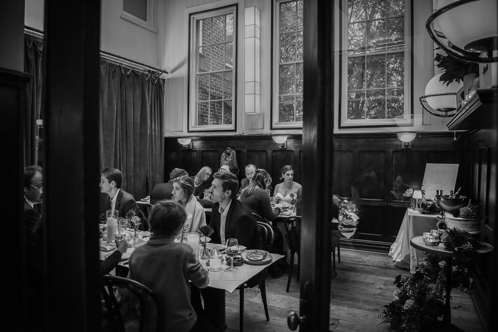 Diners enjoy meals at tables in an elegant restaurant interior with large windows and dark wood paneling.