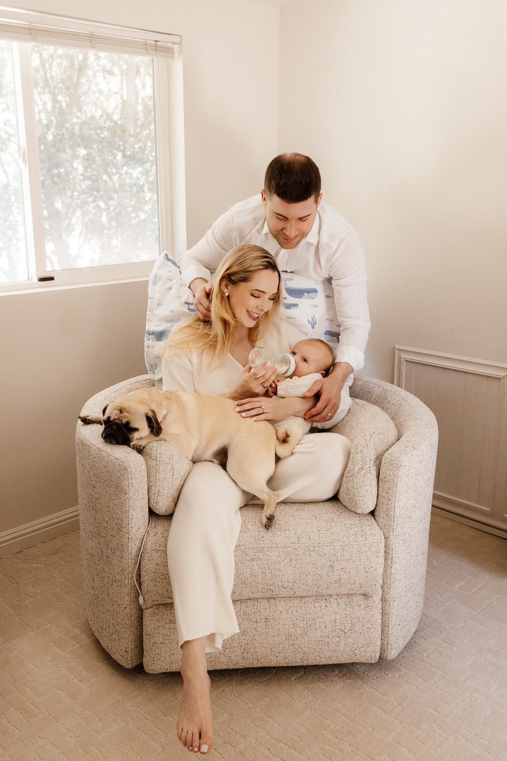 Parents smile and cuddle their newborn baby while feeding him a bottle in his Los Altos Hills nursery during their lifestyle newborn photos
