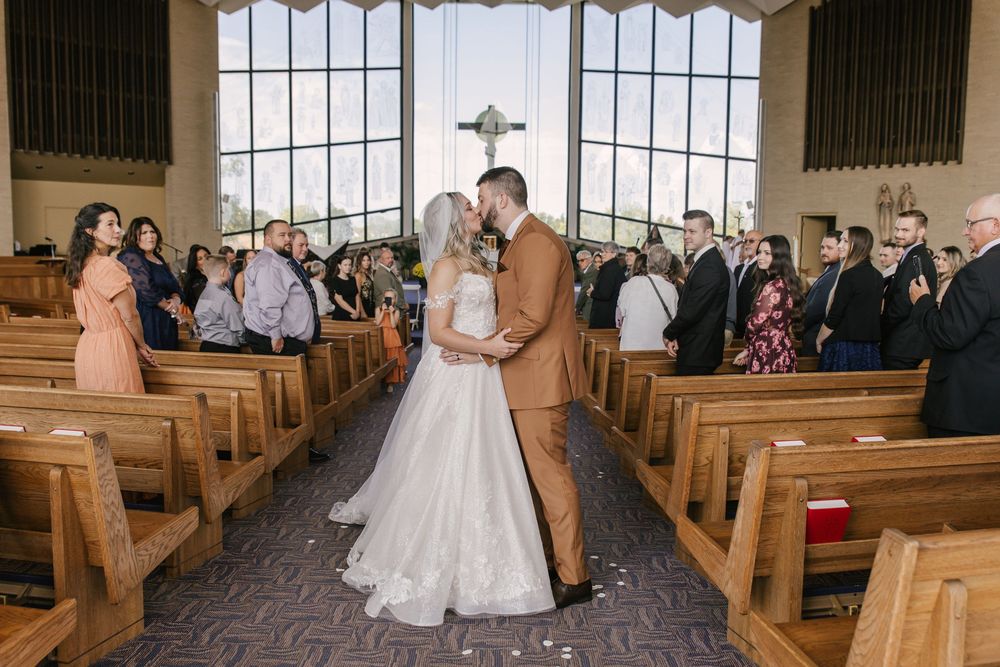 A church wedding ceremony with wooden pews and guests seated along the aisle as the couple walks together.