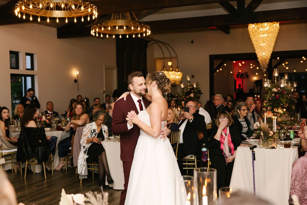 Wedding guests dancing and celebrating on a dance floor under elegant chandeliers at an evening reception.