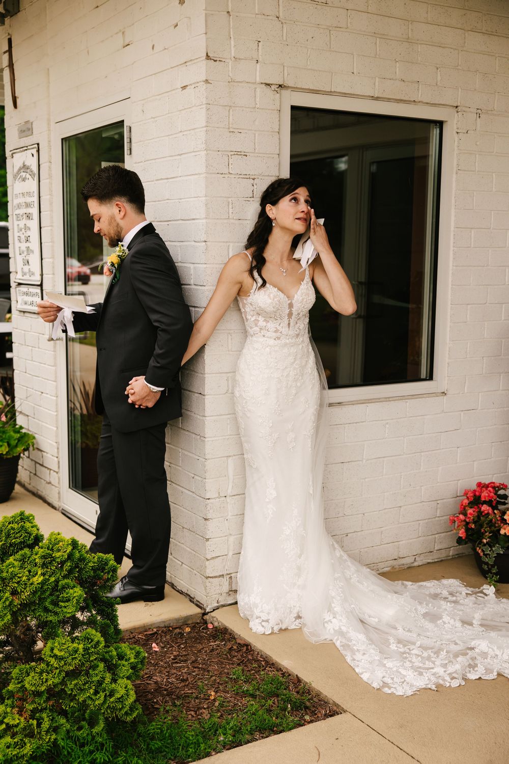 Playful wedding photo session against a white brick building with trailing lace dress details.