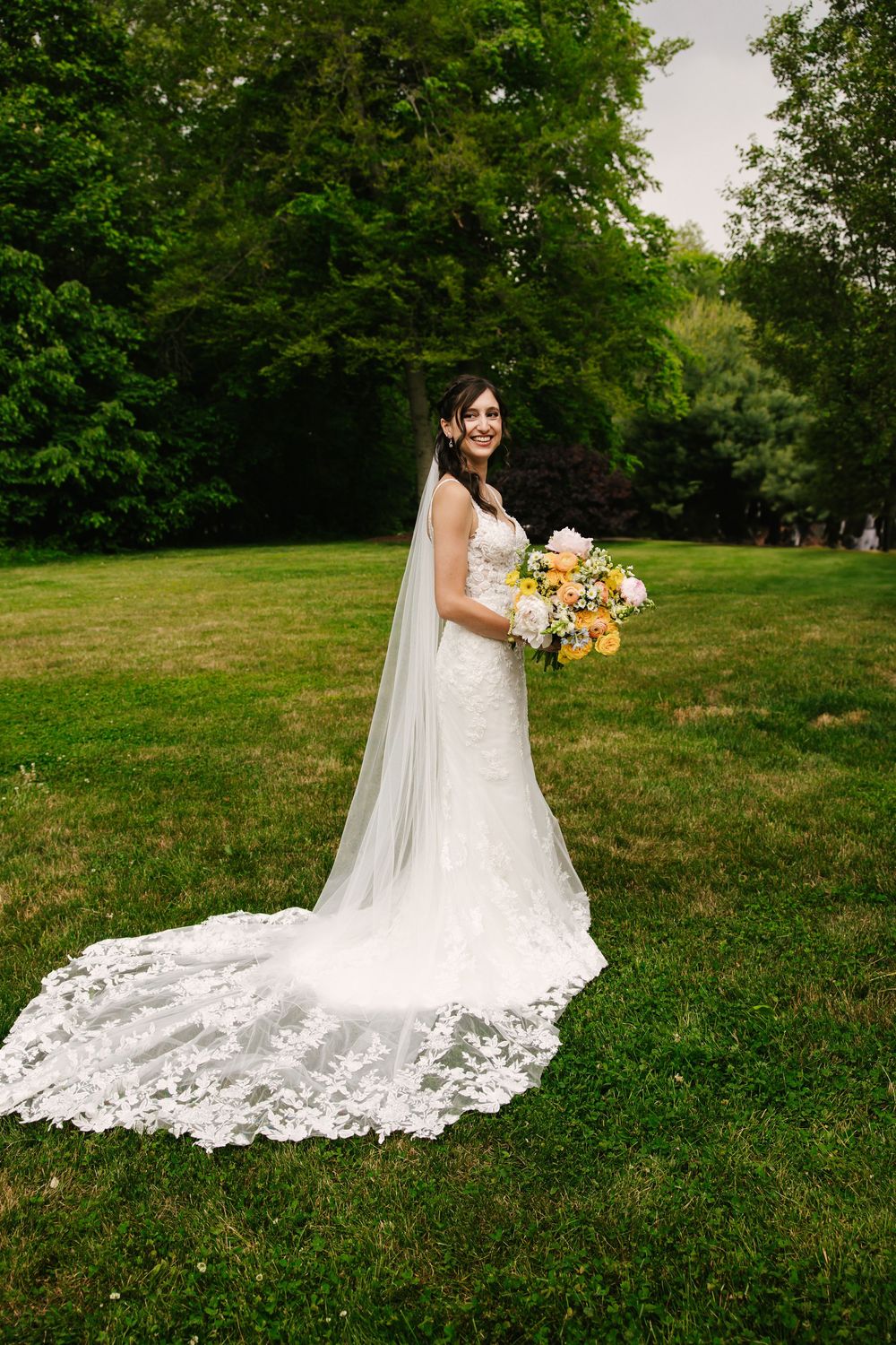 White lace wedding dress with long train spread out on green grass.