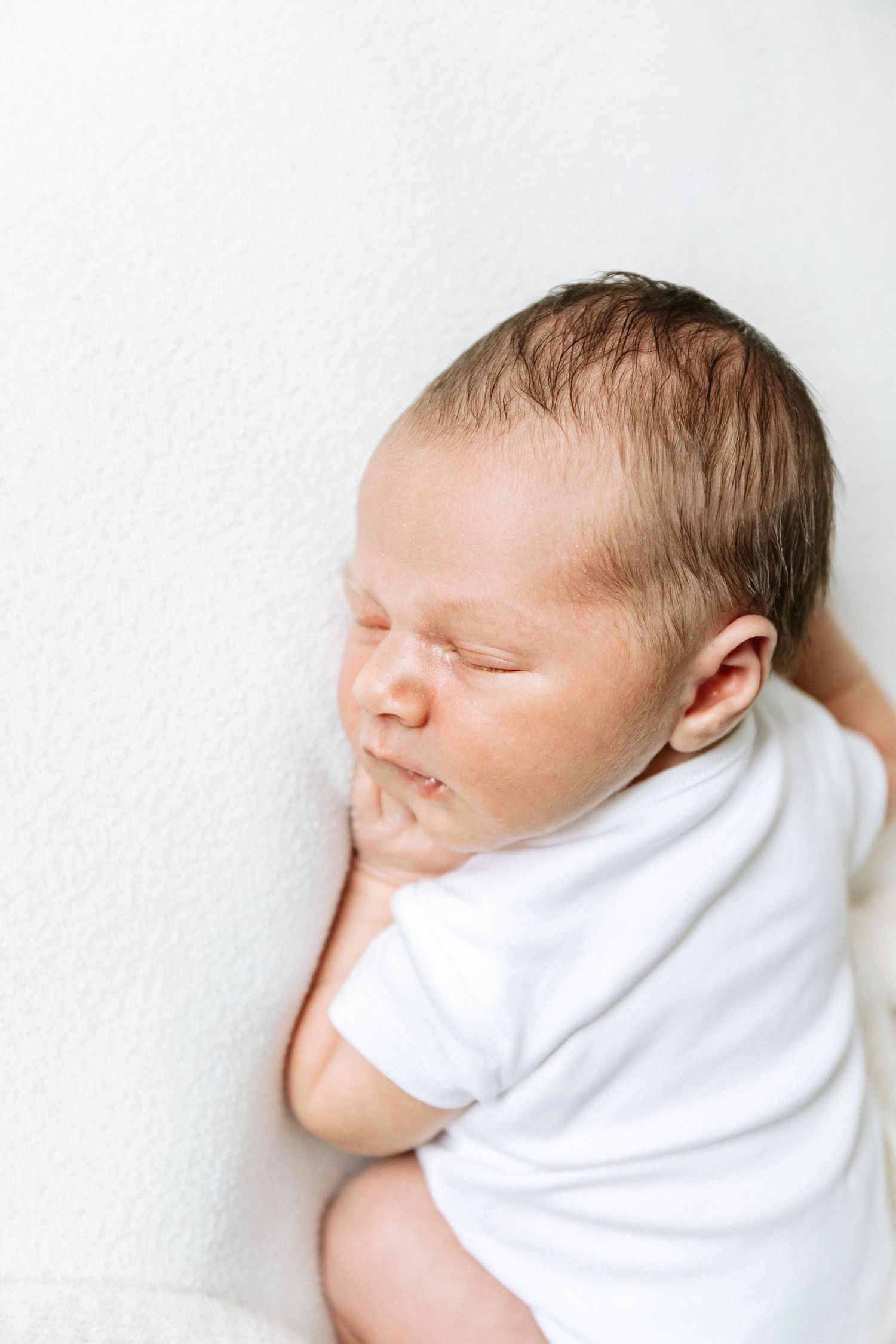 Sleeping newborn baby in soft white baby grow during professional newborn photography session  shoot in Nottingham