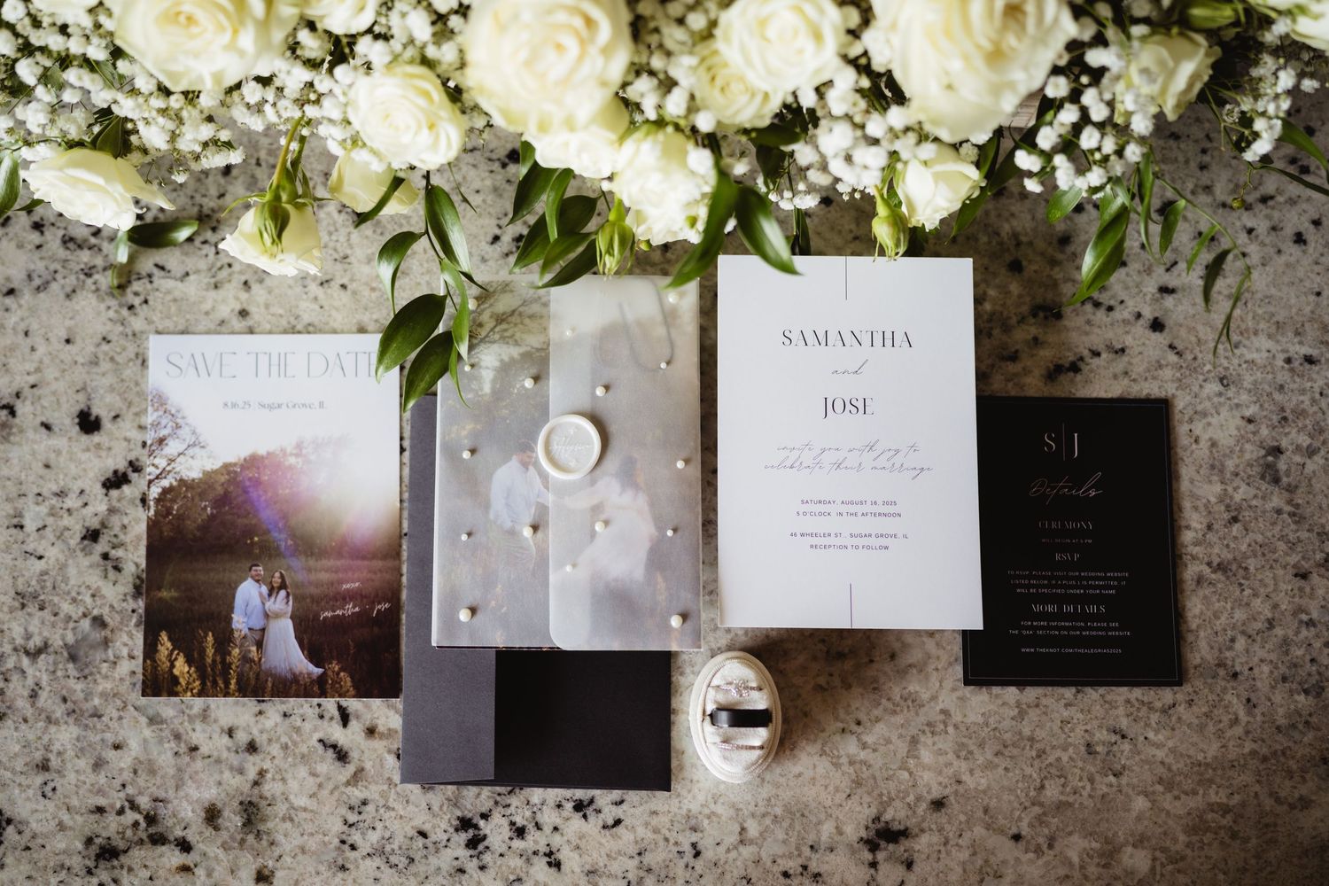 Wedding stationery and white roses displayed on a textured stone surface with elegant invitation details.