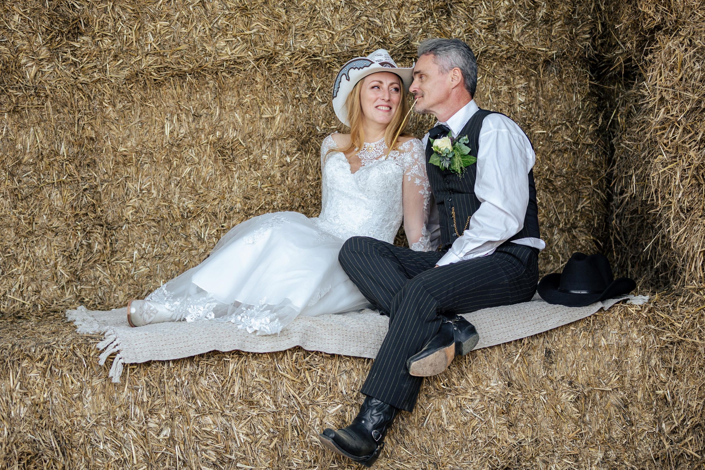 Bruidspaar zit samen op hooibalen tijdens een country en western fotoshoot