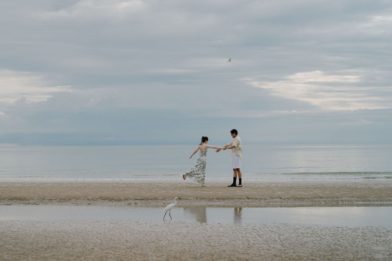 A minimalist wide shot of figures on a vast empty beach under cloudy skies.