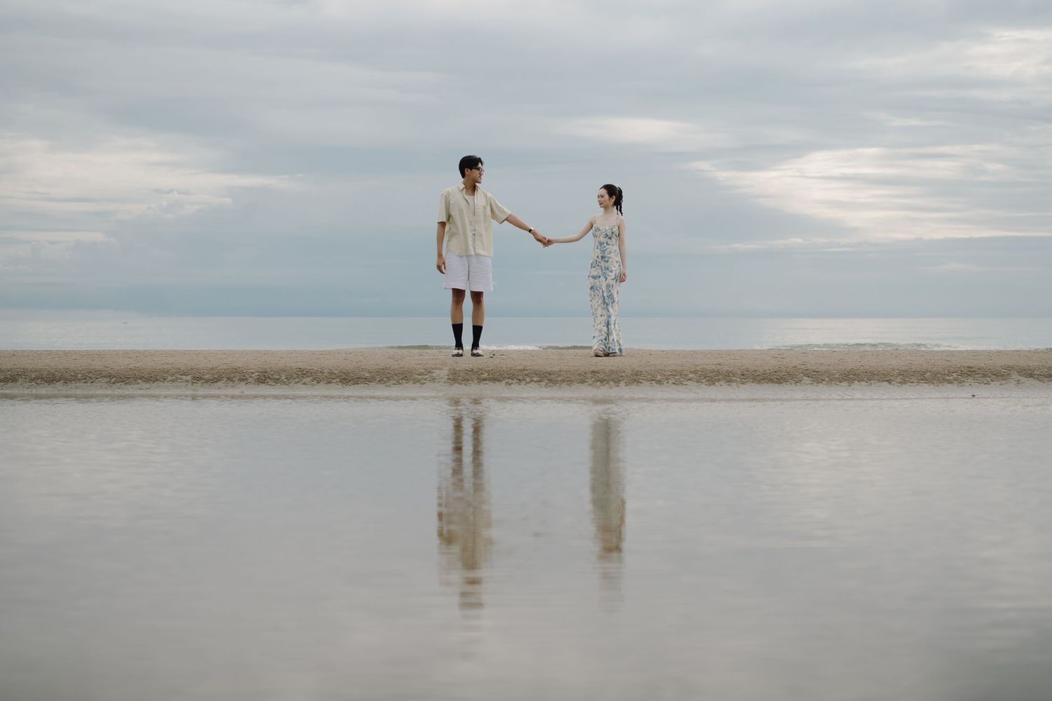 Minimalist beach landscape with tiny figures reflected in wet sand.