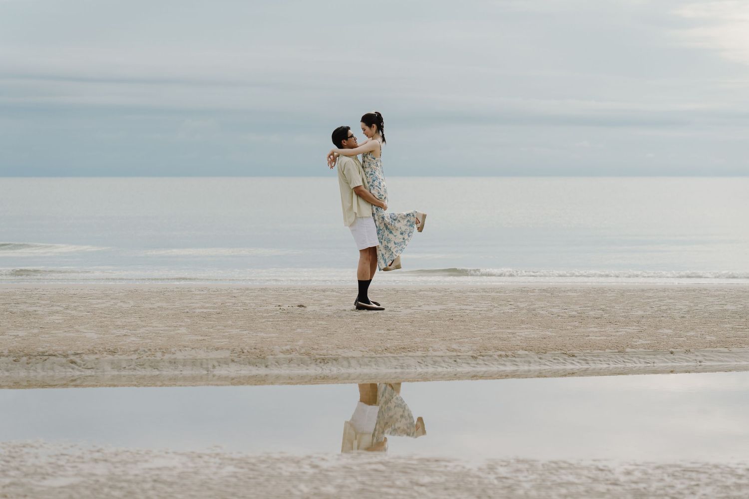 Wide beach scene with small silhouettes walking along calm shoreline.