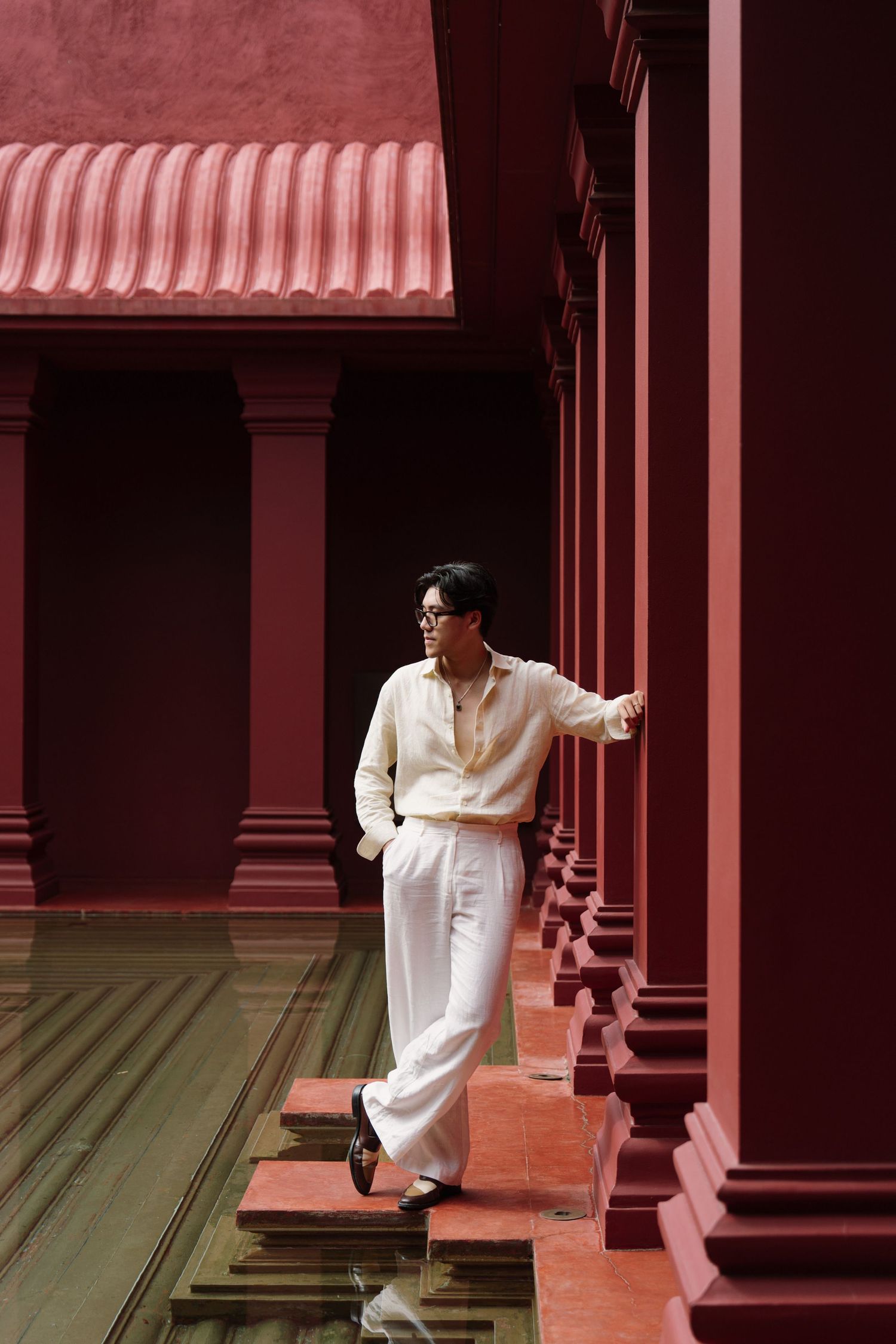 Figure moving through red-tinted colonnade with dramatic architectural elements.