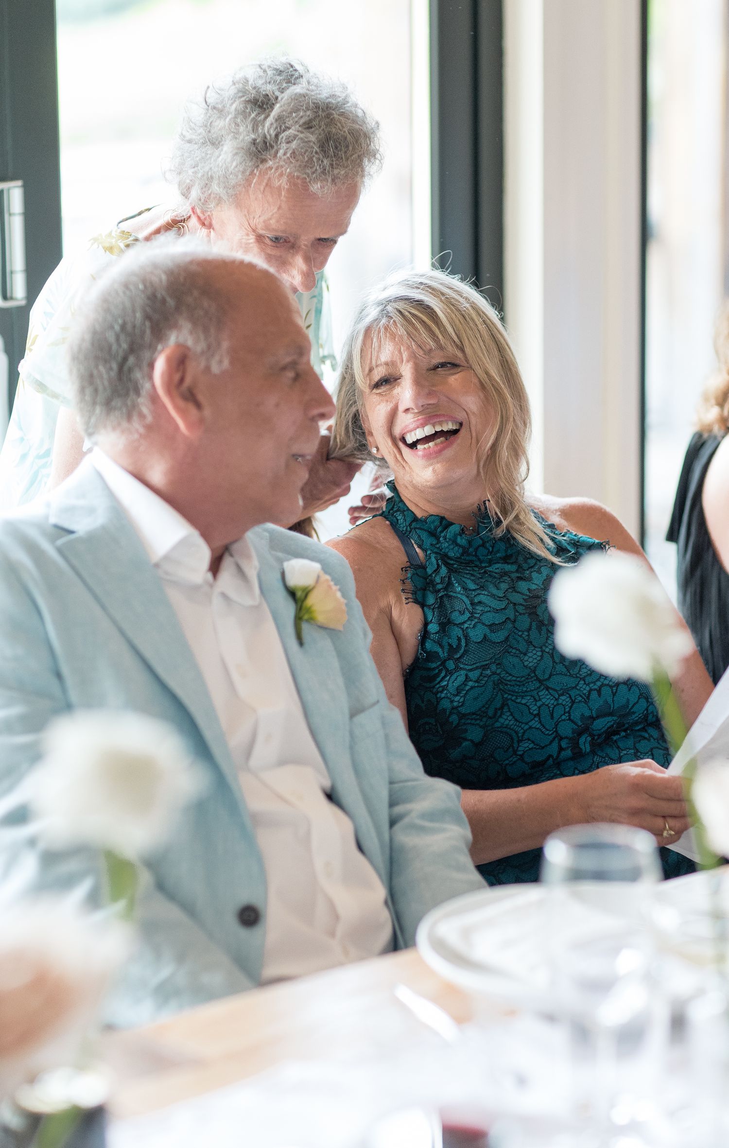 Guests share a joyful moment of laughter during a wedding reception while seated at a formal dining table.
