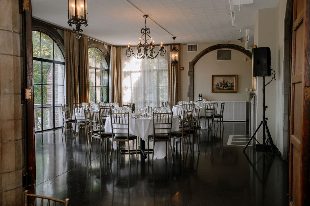 A grand ballroom interior with elegant chandeliers, stone columns and formal dining tables arranged for an event.