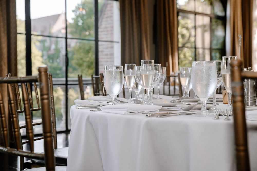 An elegant wedding reception venue with white tablecloths, tall windows and natural lighting illuminating the dining area.