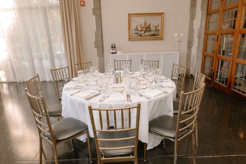 Elegant white tablecloths and silver Chiavari chairs create a sophisticated dining setup in a formal restaurant setting.