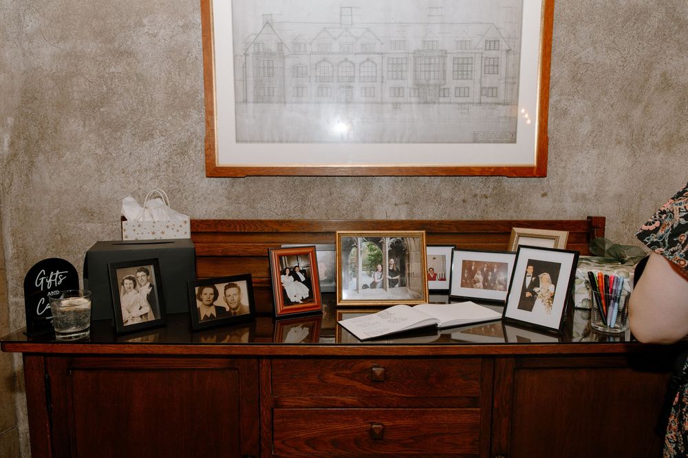 Collection of framed photographs displayed on top of a wooden dresser beneath a wall-mounted artwork in warm lighting.