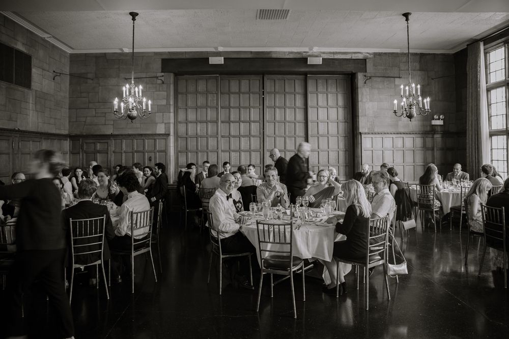 Black and white photo of a grand ballroom reception with crystal chandeliers and round tables.