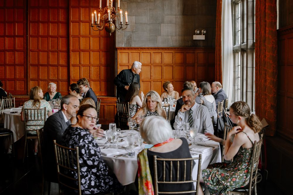 Wedding guests enjoying a formal dining experience in an elegant wood-paneled room with chandelier lighting.