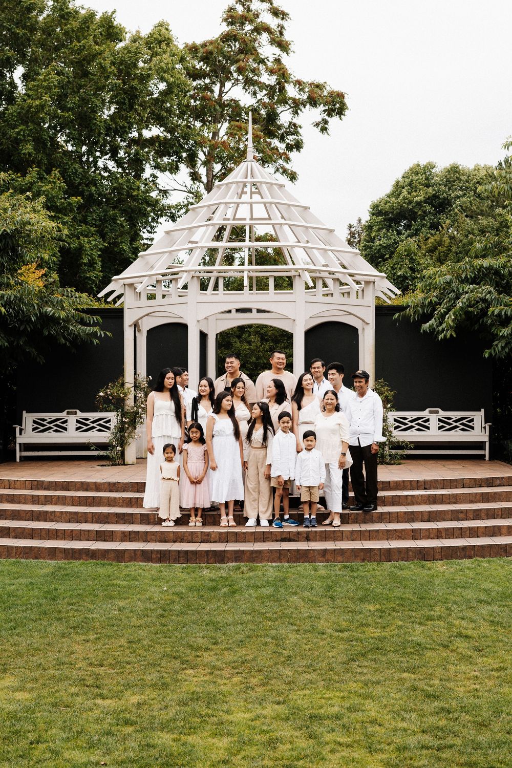 A group in white attire gathers under an elegant white gazebo in a garden setting at sunset.